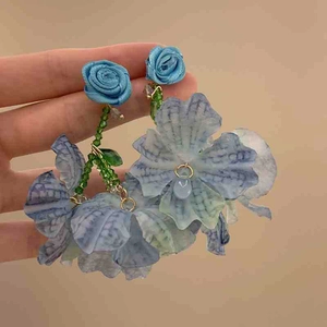Detail of handmade blue fabric flower earrings with green beads and gold wire hooks