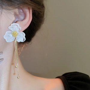 Close-up of white acrylic flower earrings with long gold tassels on a model