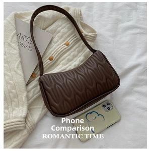Brown quilted underarm bag size comparison with a phone on a textured background