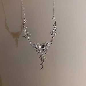 Silver butterfly necklace with thorn-like branches casting artistic shadows on grey background
