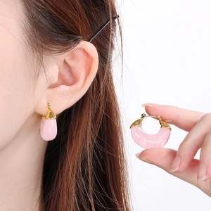 Detail of pink resin U-shaped earring with golden metal clasp shown on model