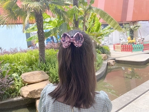 Close-up of a pink sequin bow hair clip worn by a girl against an outdoor garden background