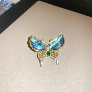 Vue détaillée d'une broche papillon en nacre bleue et cristal vert sur base dorée