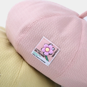 Macro detail of pink knit beret featuring waffle texture and colorful floral patch