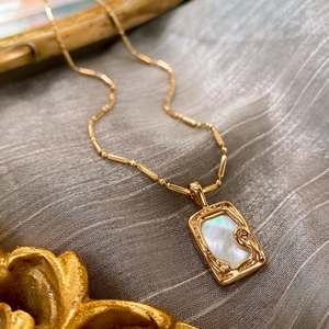 Detailed close-up of gold plated square pendant with mother of pearl inlay on fabric