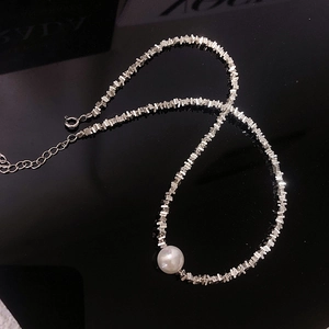 Macro detail of irregular silver bead necklace with a white pearl on black background