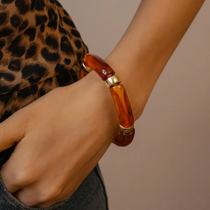 Detail of amber acrylic bracelet with gold beads worn by a model in leopard print