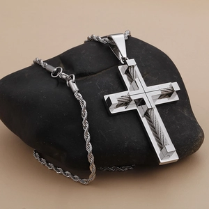 Macro view of silver stainless steel cross pendant with cable inlay on dark rock