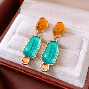 Macro view of vintage oval resin drop earrings with amber and teal stones in gold setting