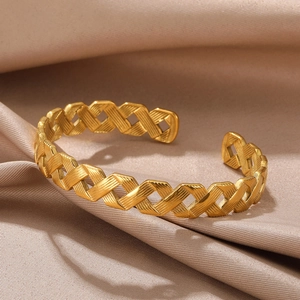 Detailed macro view of gold-plated woven texture on minimalist open bangle over silk fabric