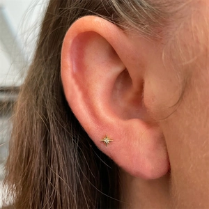 Close-up of a gold star-shaped cartilage stud with a diamond on a model's ear