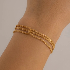 Close-up of triple-layered golden wavy chain bracelets on a woman's wrist