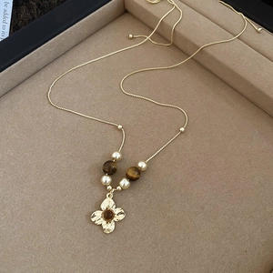 Detail of tiger eye cross pendant with pearls on a golden chain in a jewelry tray