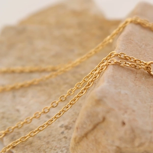 Macro shot of detailed golden linked chain necklace on a textured natural stone background