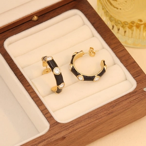 Detail of gold C-shaped earrings with black enamel and crystals in a wooden box