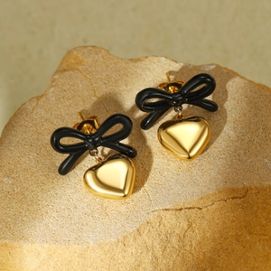 Close-up of black bow and gold heart drop earrings on natural stone background