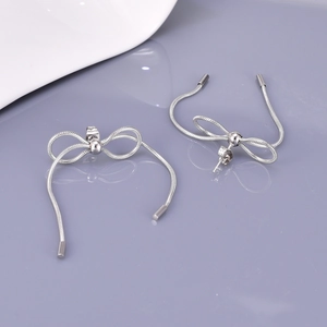 Detail of silver bow earrings with metal snake bone chain tassels on light background