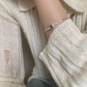 Detail of silver bangle with oval dark gemstone on a minimalist knitwear sleeve