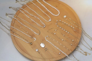 Detailed view of white pearl necklaces with gold heart and moon pendants on wood tray