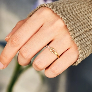 Macro view of a two-tone silver and gold knot ring worn on a finger with knitwear