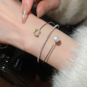Detail of layered silver floral bangle with yellow gemstone and white pearl on wrist