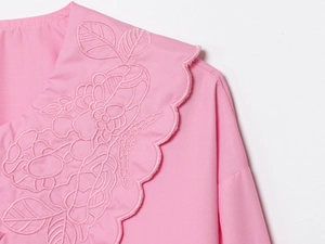 Detail of pink blouse collar featuring floral embroidery and hollow-out lace edges