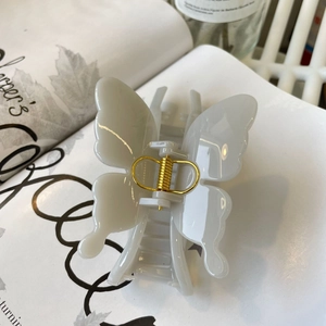 Detail of a creamy white butterfly hair claw clip with golden metal spring on a magazine