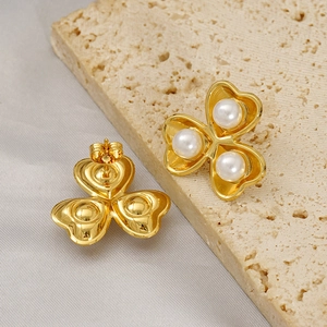 Gold vintage clover leaf earrings with white pearls on a textured stone display