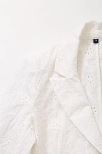 Close-up of white blazer collar featuring intricate floral hollow embroidery and stitching