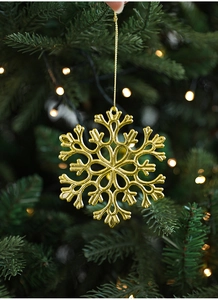 Golden snowflake ornament hanging on Christmas tree with warm bokeh lighting detail