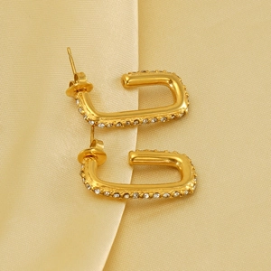 Macro shot of 18K gold plated U-shaped earrings with zircon inlay on silk background