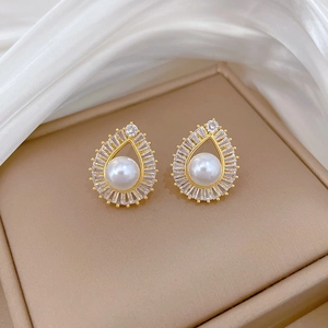 Macro shot of gold teardrop earrings with central pearl and zircon accents on silk