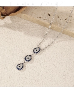Macro shot of silver Y-chain necklace with blue teardrop evil eye pendants on stone