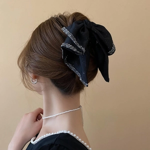 Close-up of a large black fabric bow hair claw with shimmering silver rhinestones on a model