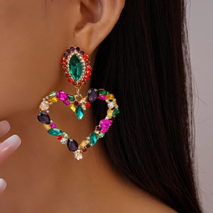 Close-up of a model wearing large heart-shaped drop earrings with colorful rhinestones