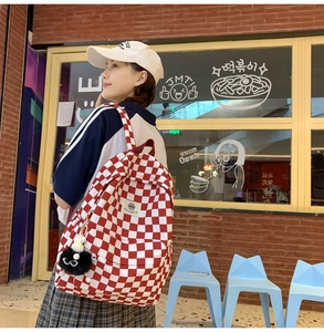 Side view of red and white checkerboard canvas backpack with cute black plush pendant