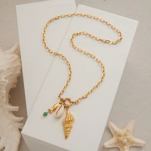Détail du collier doré avec pendentifs coquillage et poisson sur des blocs blancs épurés