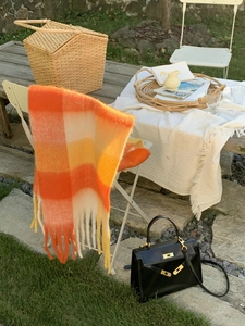 Detailed close-up of orange and yellow plaid tassel scarf draped on a chair outdoors