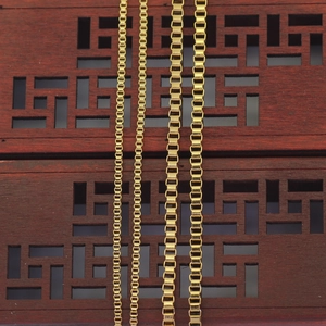 Detail of four golden stainless steel box chains on dark wood surface showing texture