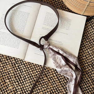 Detail of a thin brown leather belt paired with a paisley printed silk scarf on a book