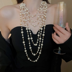 Close-up of elegant layered pearl necklace on model in black dress with champagne glass
