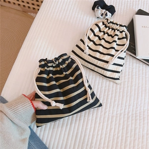 Detail of striped cotton drawstring pouches in black and beige on a cozy textured background