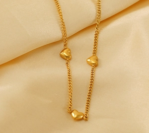Detalle de tres colgantes de corazón dorados en un collar sobre una tela de seda beige