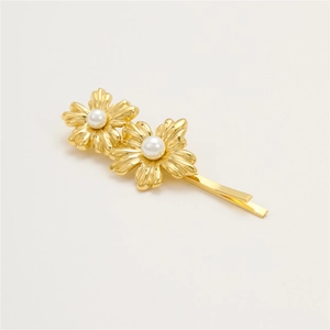 Detail of a golden floral hair clip with white pearls on a minimalist background