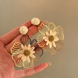 Detail view of handmade raffia flower drop earrings with golden metal petals