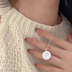Detail view of 925 silver evil eye coin necklace worn on a beige knit sweater texture