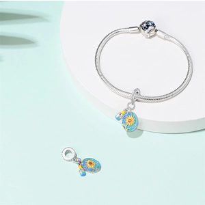 Detailed close-up of silver snake chain bracelet with blue sunflower and brush charms