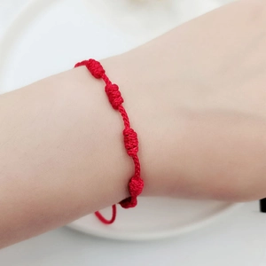 Detail of red handmade woven cord bracelet with knots worn on a wrist over white background