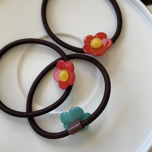 Détail de trois élastiques à cheveux fleurs rouge et vert sur une assiette en céramique