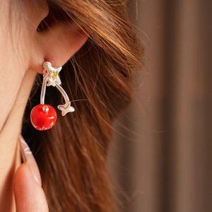 Macro view of cherry-shaped silver stud earrings with red enamel and yellow gems on model